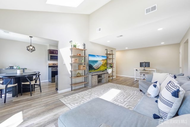 living room featuring baseboards, a high ceiling, light wood-type flooring, and visible vents