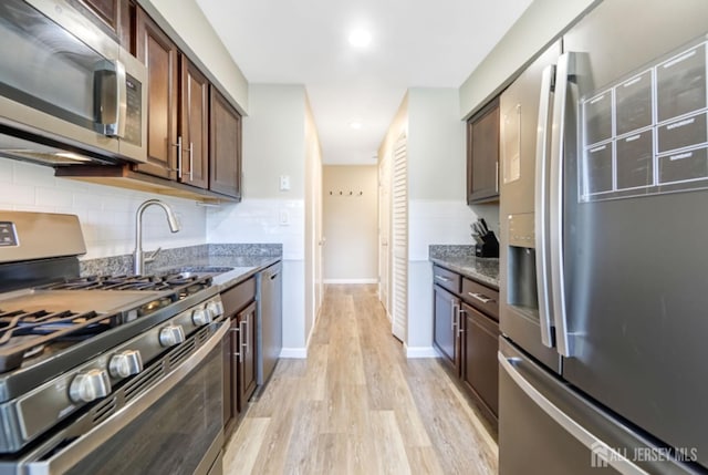 kitchen with appliances with stainless steel finishes, a sink, light wood-style flooring, stone counters, and backsplash