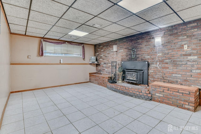 14 Bradford Rd, East Brunswick, NJ 08816 - unfurnished living room featuring a wood stove, baseboards, a drop ceiling, brick wall, and tile patterned flooring