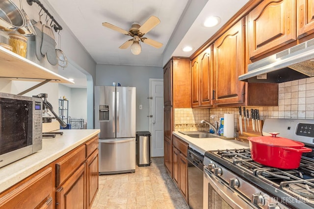 kitchen with a sink, under cabinet range hood, a ceiling fan, appliances with stainless steel finishes, and backsplash