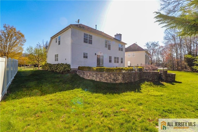 rear view of property with a lawn, a chimney, and fence