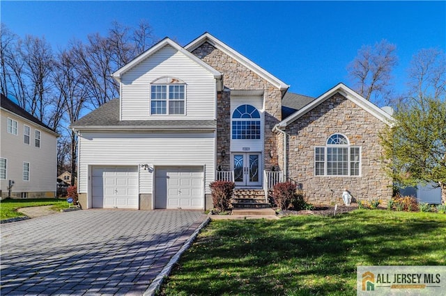 traditional-style house featuring decorative driveway, stone siding, french doors, a front yard, and a garage