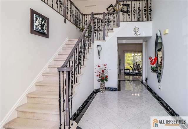 entryway featuring baseboards, marble finish floor, a towering ceiling, and stairway