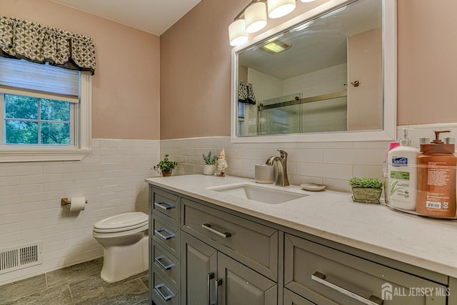 bathroom featuring vanity, toilet, a shower with door, and tile walls