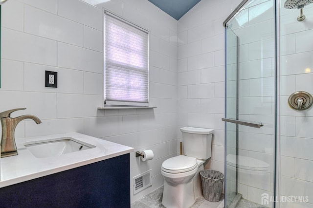 bathroom with vanity, toilet, a shower with door, and tile walls