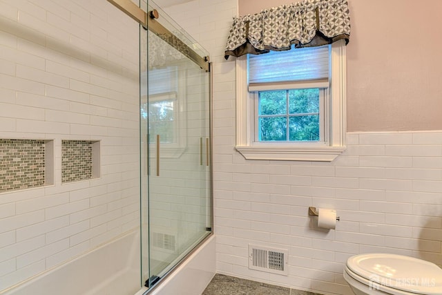 bathroom with toilet, combined bath / shower with glass door, and tile walls