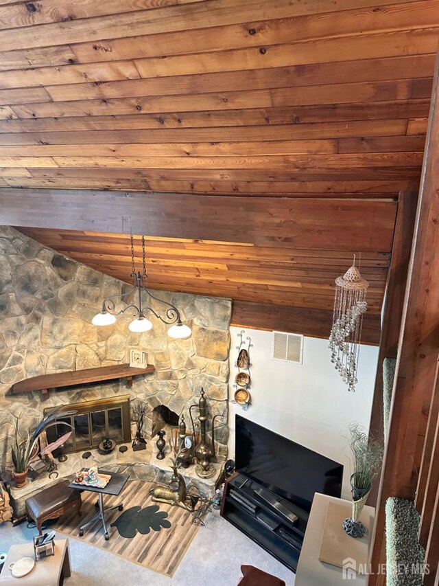 living room featuring carpet flooring, a notable chandelier, a stone fireplace, and wooden ceiling