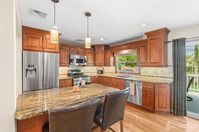 kitchen with appliances with stainless steel finishes, plenty of natural light, light wood finished floors, light stone counters, and recessed lighting