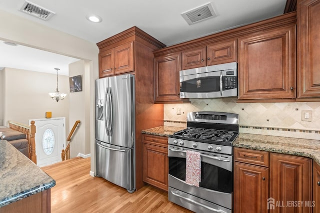 kitchen featuring stainless steel appliances, light wood-style floors, brown cabinetry, backsplash, and a chandelier