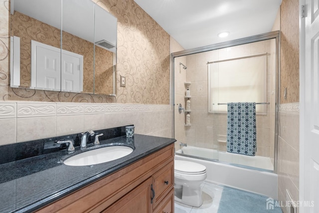 bathroom with tile walls, combined bath / shower with glass door, vanity, toilet, and tile patterned floors