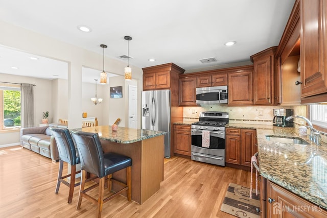 kitchen with appliances with stainless steel finishes, a sink, a breakfast bar, light wood-style floors, and stone counters