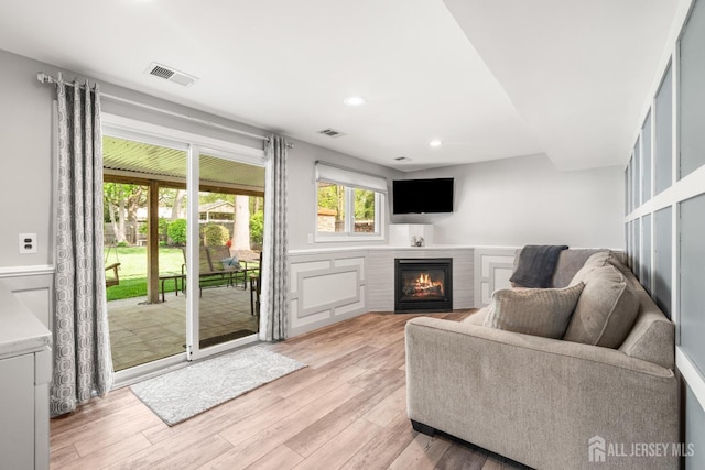 living area with a glass covered fireplace, recessed lighting, light wood-type flooring, a wainscoted wall, and a decorative wall