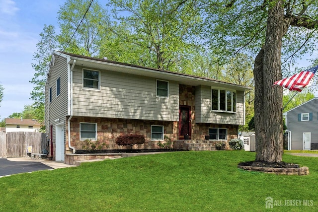 raised ranch featuring asphalt driveway, an attached garage, and stone siding