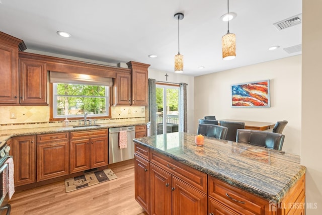 kitchen featuring appliances with stainless steel finishes, a sink, light wood finished floors, stone countertops, and decorative backsplash
