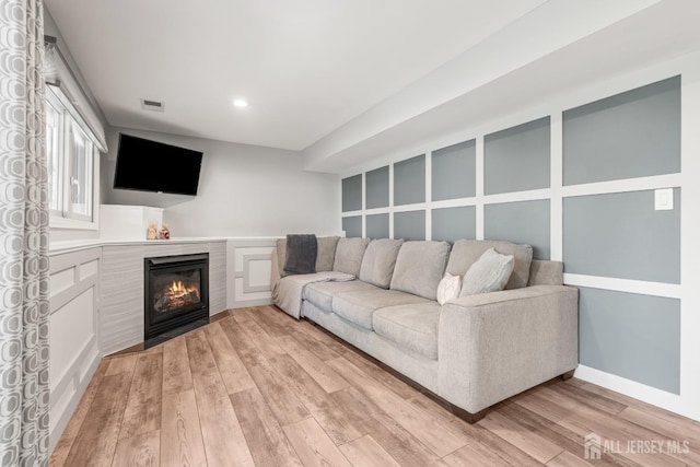 living area featuring light wood finished floors, a glass covered fireplace, and recessed lighting