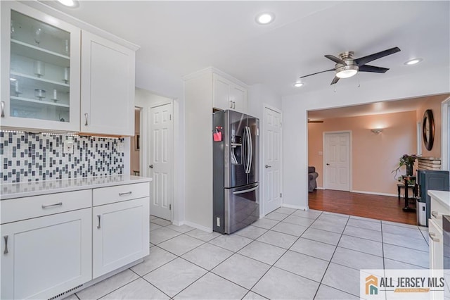 kitchen featuring light tile patterned floors, ceiling fan, white cabinetry, stainless steel fridge with ice dispenser, and decorative backsplash