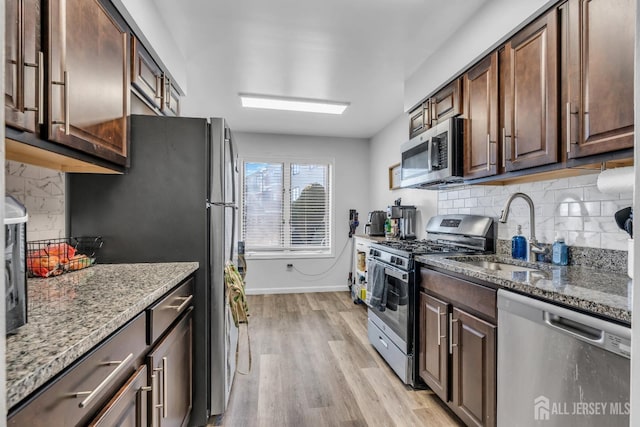 kitchen with light wood finished floors, stone countertops, appliances with stainless steel finishes, and a sink