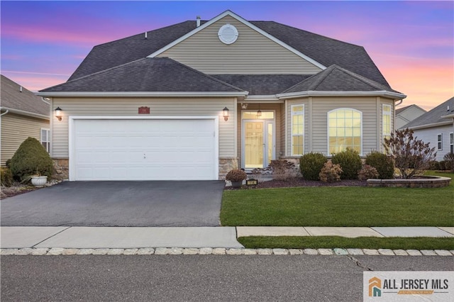 view of front of home with driveway, stone siding, a garage, and a yard