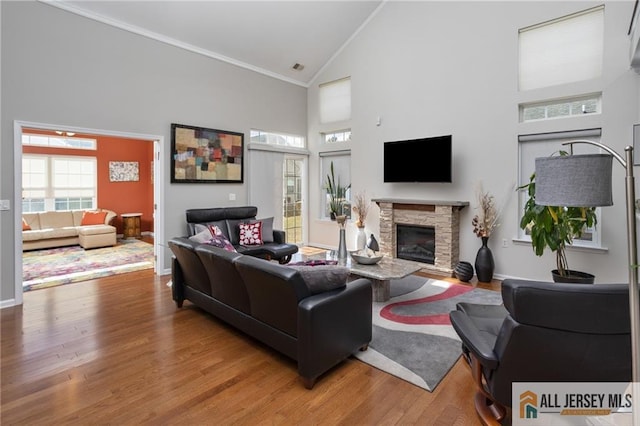 living area with high vaulted ceiling, a fireplace, baseboards, light wood finished floors, and crown molding