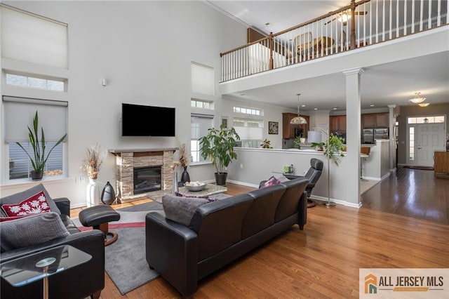 living area featuring a fireplace, wood finished floors, decorative columns, and baseboards