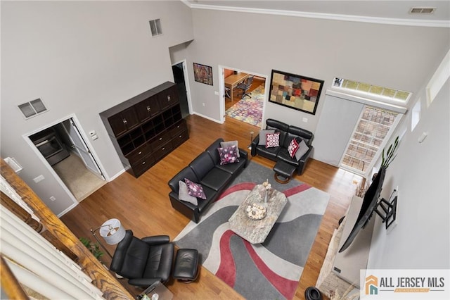 living room featuring a high ceiling, wood finished floors, visible vents, and crown molding