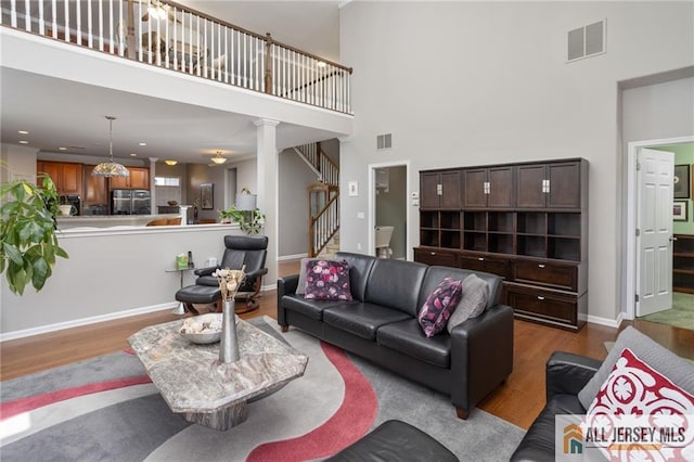 living room with a towering ceiling, stairway, visible vents, and wood finished floors