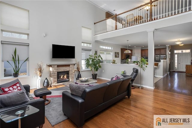 living room featuring baseboards, a towering ceiling, wood finished floors, a stone fireplace, and ornate columns