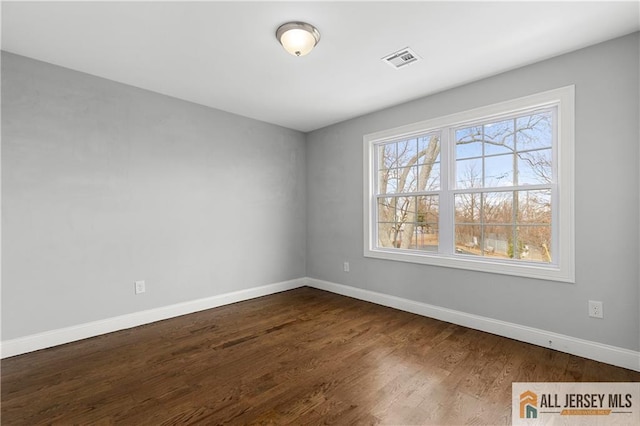 unfurnished room with visible vents, baseboards, and dark wood finished floors