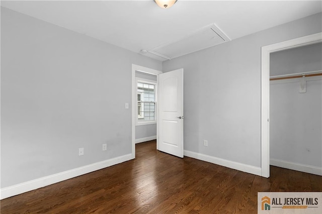 unfurnished bedroom featuring a closet, baseboards, attic access, and wood finished floors