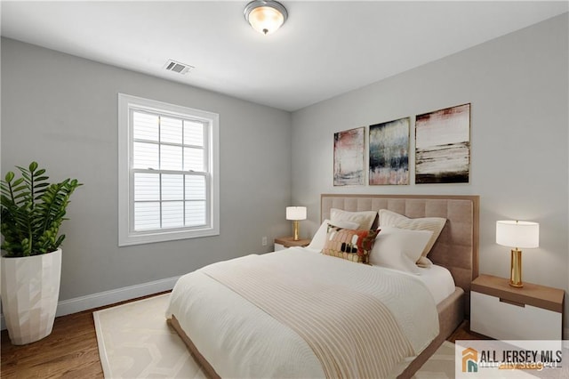 bedroom with wood finished floors, visible vents, and baseboards