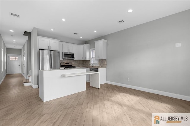 kitchen with visible vents, light wood-style flooring, stainless steel appliances, and decorative backsplash