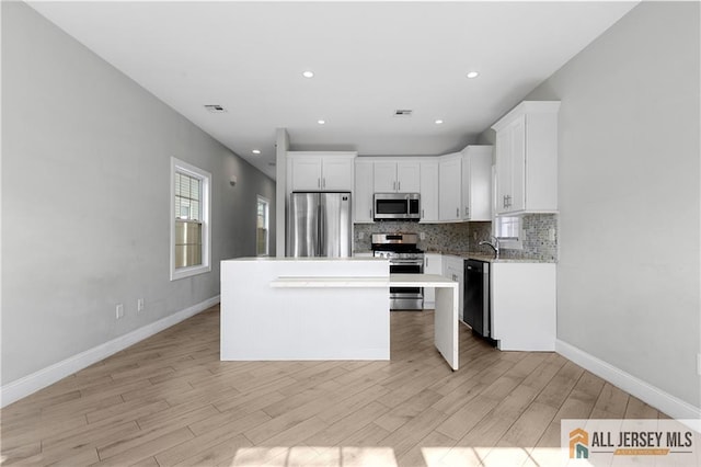 kitchen with light wood-style flooring, stainless steel appliances, decorative backsplash, white cabinets, and a center island