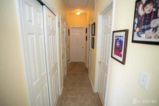 hallway featuring dark tile patterned floors and visible vents