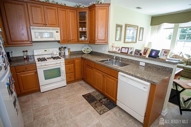 kitchen featuring brown cabinetry, a sink, a peninsula, and white appliances