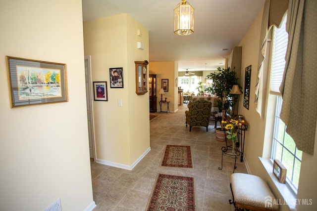 hallway featuring baseboards, light tile patterned flooring, and a chandelier