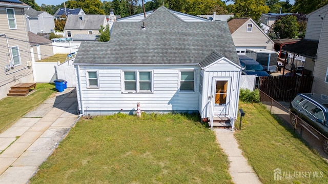 back of house with a shingled roof, a lawn, entry steps, fence, and driveway