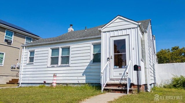 bungalow-style home with roof with shingles, a front lawn, board and batten siding, and a chimney