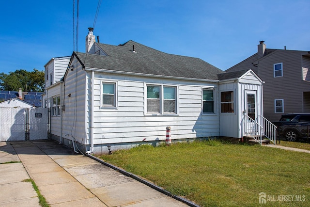 bungalow-style home featuring roof with shingles, a chimney, entry steps, a gate, and a front lawn