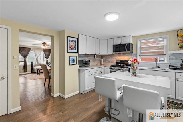 kitchen featuring stainless steel appliances, a sink, a breakfast bar area, decorative backsplash, and dark wood-style flooring