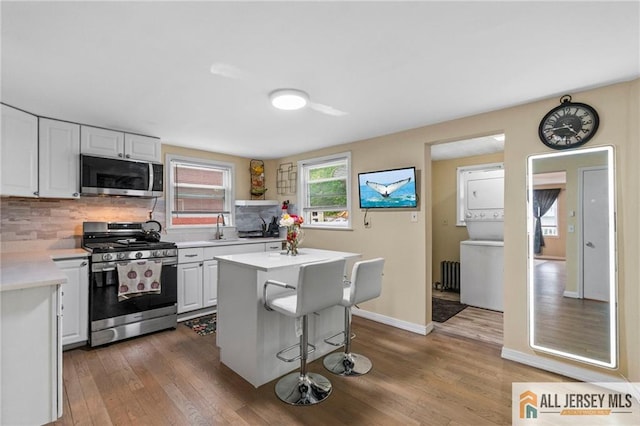 kitchen with stainless steel appliances, stacked washer and clothes dryer, light countertops, a sink, and wood finished floors