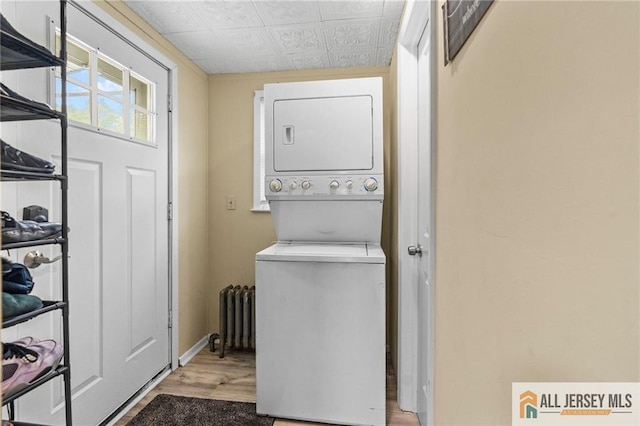 laundry area with stacked washer and clothes dryer, an ornate ceiling, radiator heating unit, wood finished floors, and baseboards