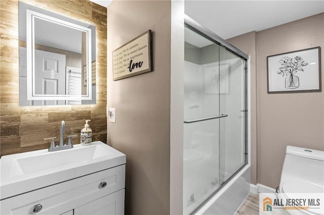 full bath with toilet, vanity, bath / shower combo with glass door, and wood finished floors