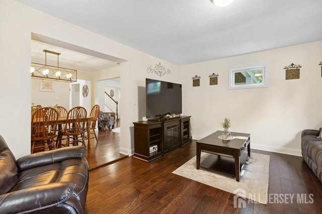 living room featuring baseboards, a notable chandelier, wood finished floors, and stairs