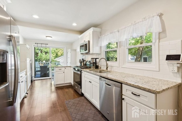 kitchen featuring light stone countertops, appliances with stainless steel finishes, a peninsula, dark wood-style floors, and a sink