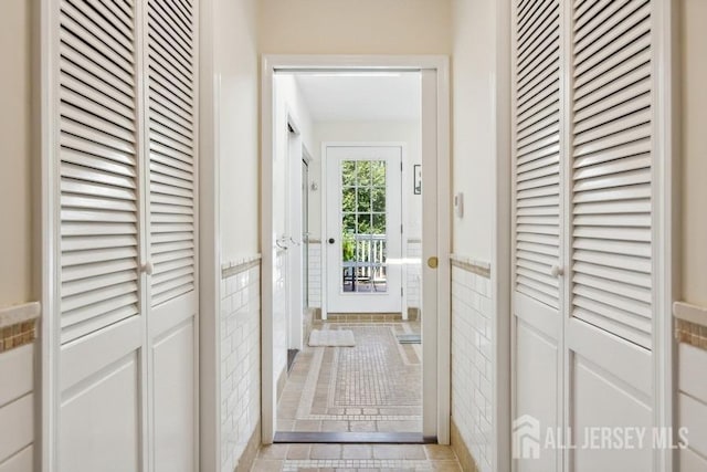 doorway with tile patterned flooring, tile walls, and a wainscoted wall