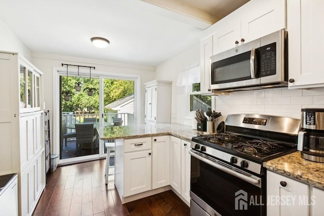 kitchen with a peninsula, dark wood-style flooring, decorative backsplash, white cabinets, and appliances with stainless steel finishes