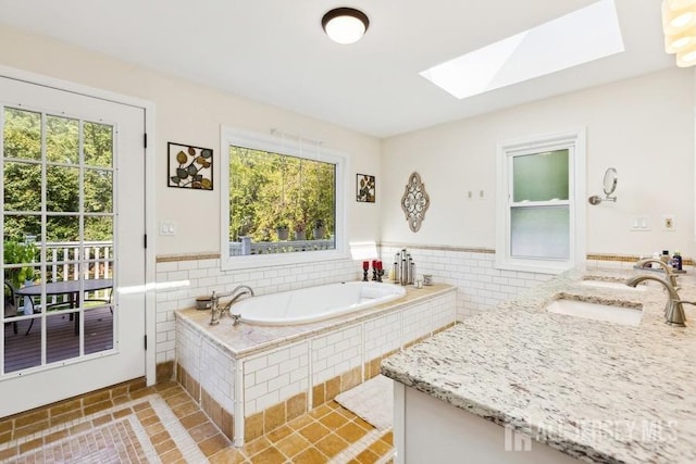 full bathroom with a wainscoted wall, a garden tub, tile walls, a skylight, and vanity