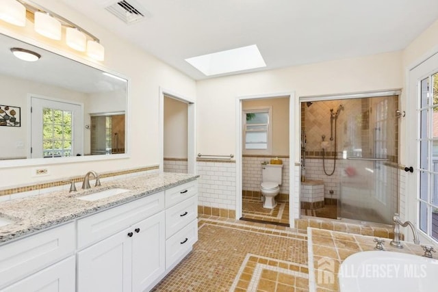 full bathroom with visible vents, wainscoting, a stall shower, a skylight, and tile walls