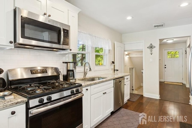 kitchen featuring visible vents, dark wood-type flooring, a sink, stainless steel appliances, and decorative backsplash