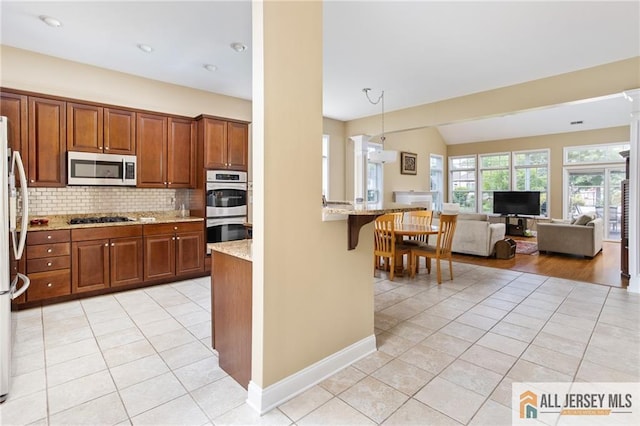 kitchen with light tile patterned floors, light stone counters, stainless steel appliances, a breakfast bar, and tasteful backsplash